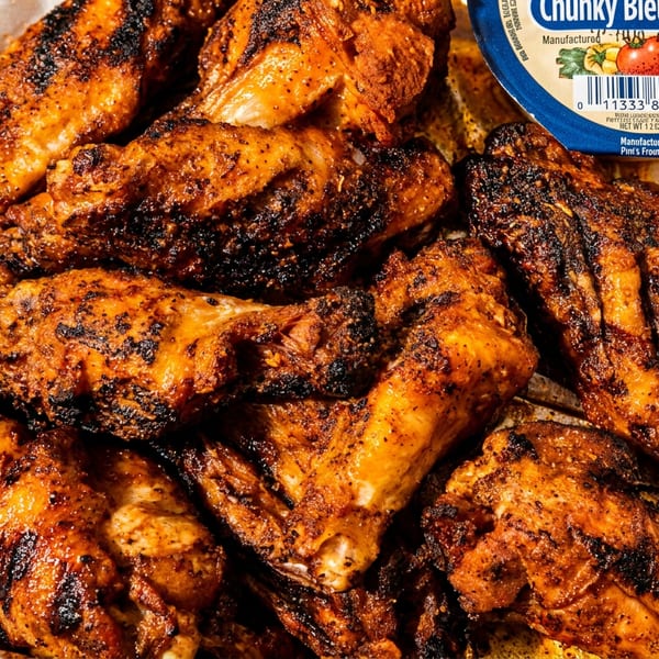 Grilled chicken wings with a side of Chunky Bleu Cheese dressing in a foil-lined container.