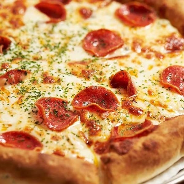 Close-up of a pepperoni pizza with melted cheese and sprinkled herbs on a metal tray.