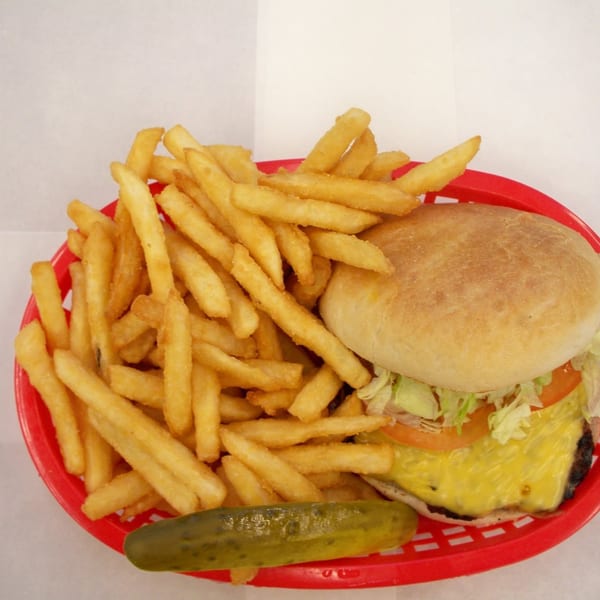 A cheeseburger with lettuce and tomato, a pile of fries, and a pickle spear in a red basket.